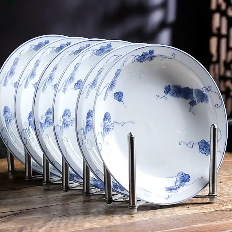 Set of six white porcelain vegetable plates with delicate blue floral patterns displayed on a metal stand