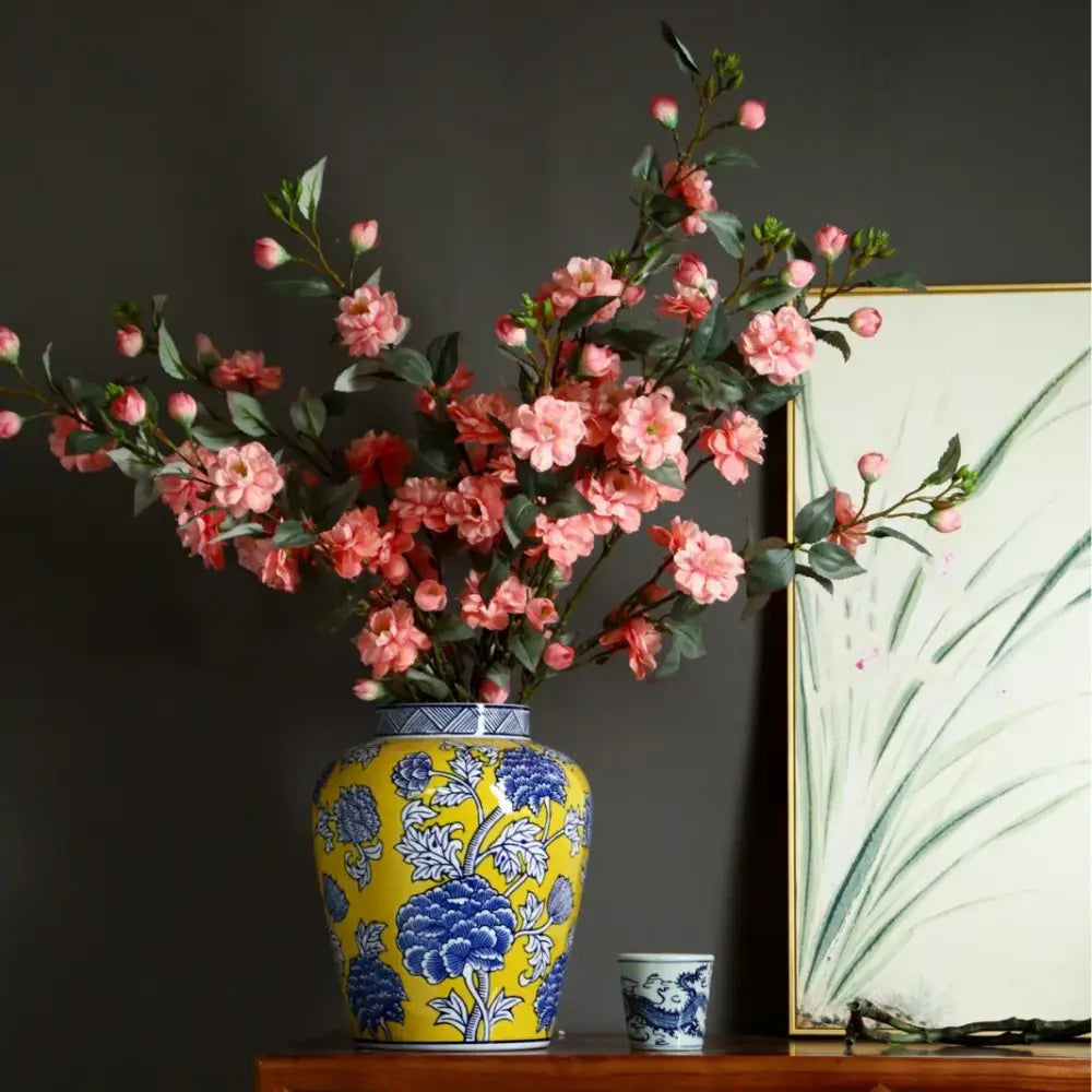A vibrant yellow ceramic decorbites chinese blue white porcelain vase with blue floral patterns holding pink blossoms