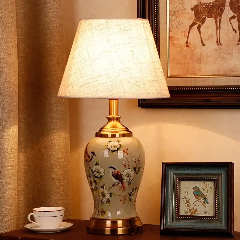 Cream-colored DecorBites™ ceramic table lamp with gold-toned metal base and hand-painted floral and bird motifs