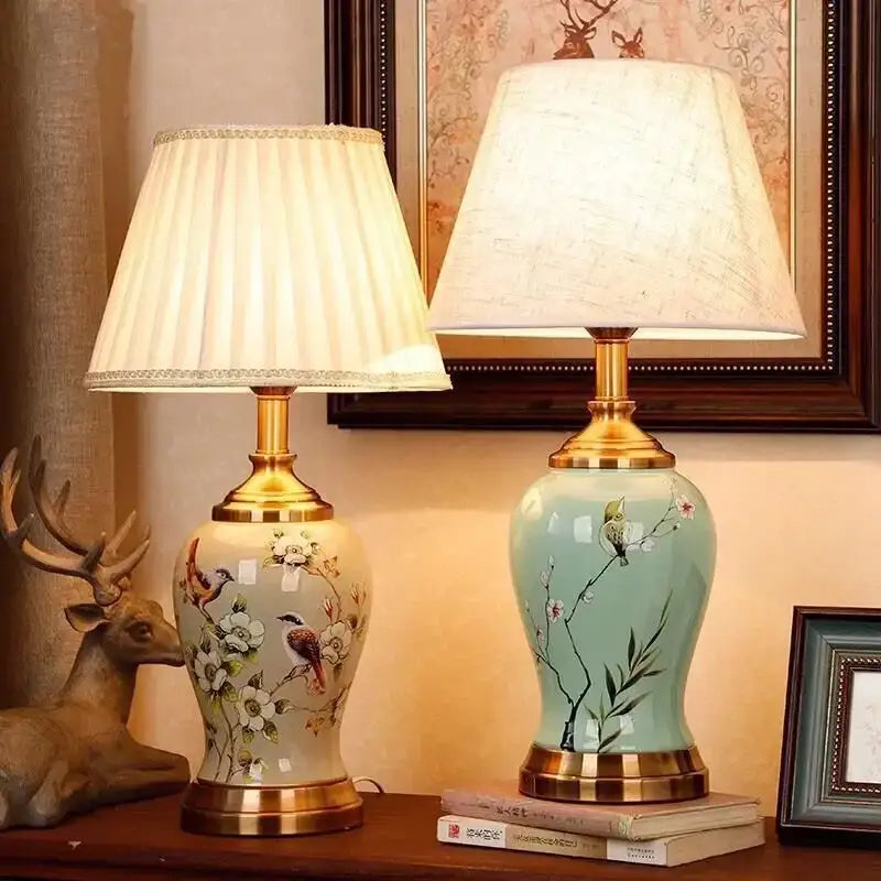 Two ceramic table lamps with gold metal bases featuring cream and light blue glazes with bird and floral motifs