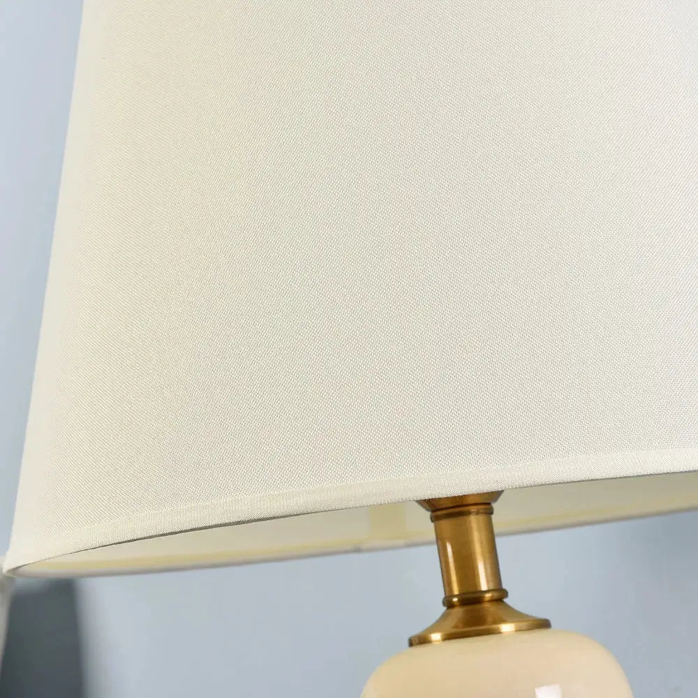 Cream-colored fabric lampshade with woven texture on brass stem in decorbites™ ceramic table lamps for living room decor