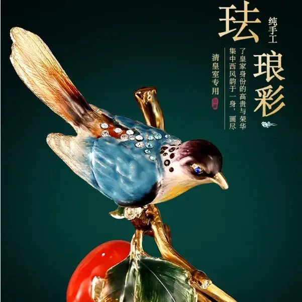 A handcrafted blue and gold enamel persimmon ruyi bird figurine with rhinestones perched beside a red fruit for décor