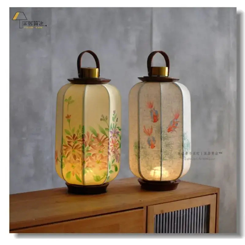 Two illuminated hexagonal decorbites chinese fabric desk lamps with hand-painted floral and fish motifs in warm tones