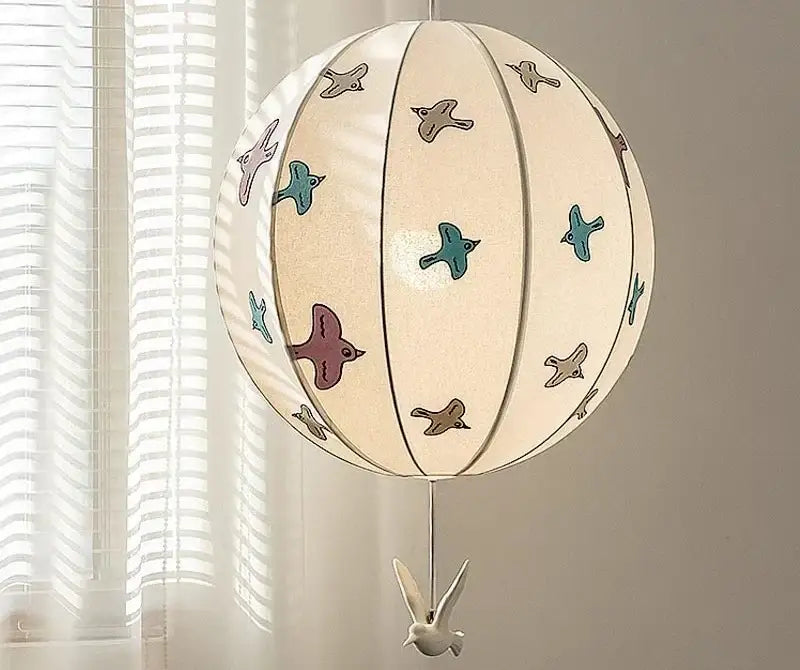 A cream-colored spherical paper pendant light with colorful bird illustrations and a white bird ornament decorbites chinese medieval dove
