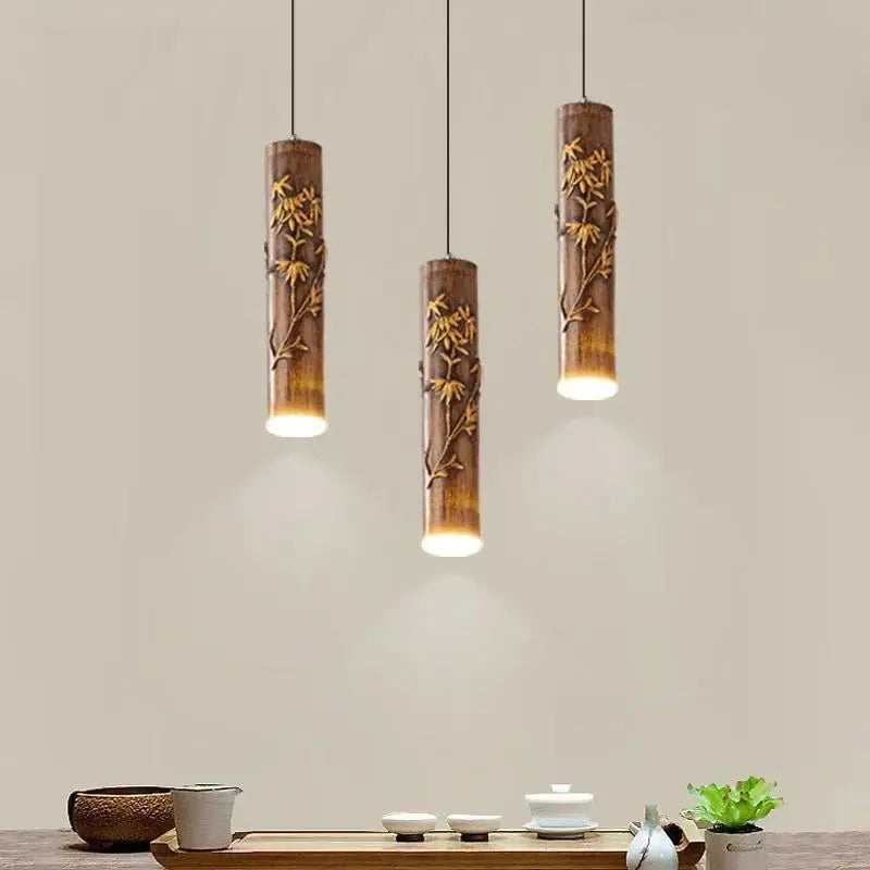 Three cylindrical bamboo pendant lights with golden leaf carvings and warm glow by DecorBites Chinese modern art