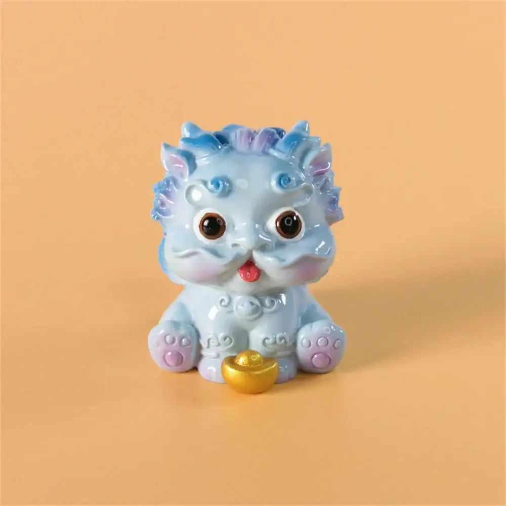 A charming light blue ceramic mythology lion figurine with purple accents and brown eyes beside a small golden ingot