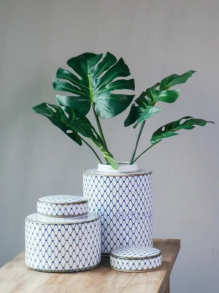 White ceramic decorbites chinese retro canister with blue diamond pattern gold trim holding green monstera leaves
