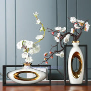 Two modern ceramic vases with gold accents holding white blossoms in a decorbites chinese style ceramic wooden frame