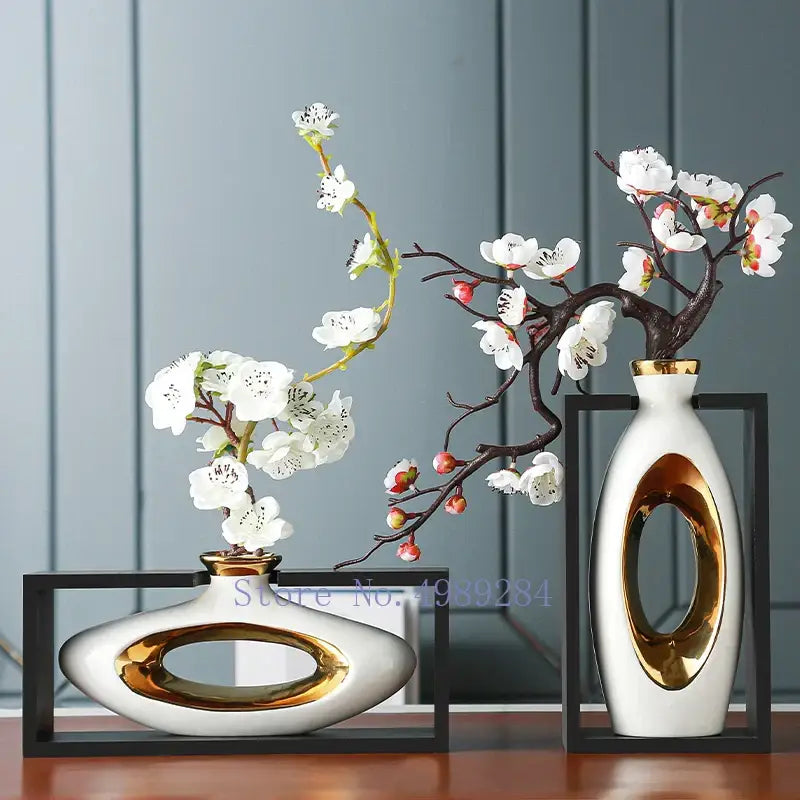 Two modern ceramic vases with gold accents holding white blossoms in a decorbites chinese style ceramic wooden frame
