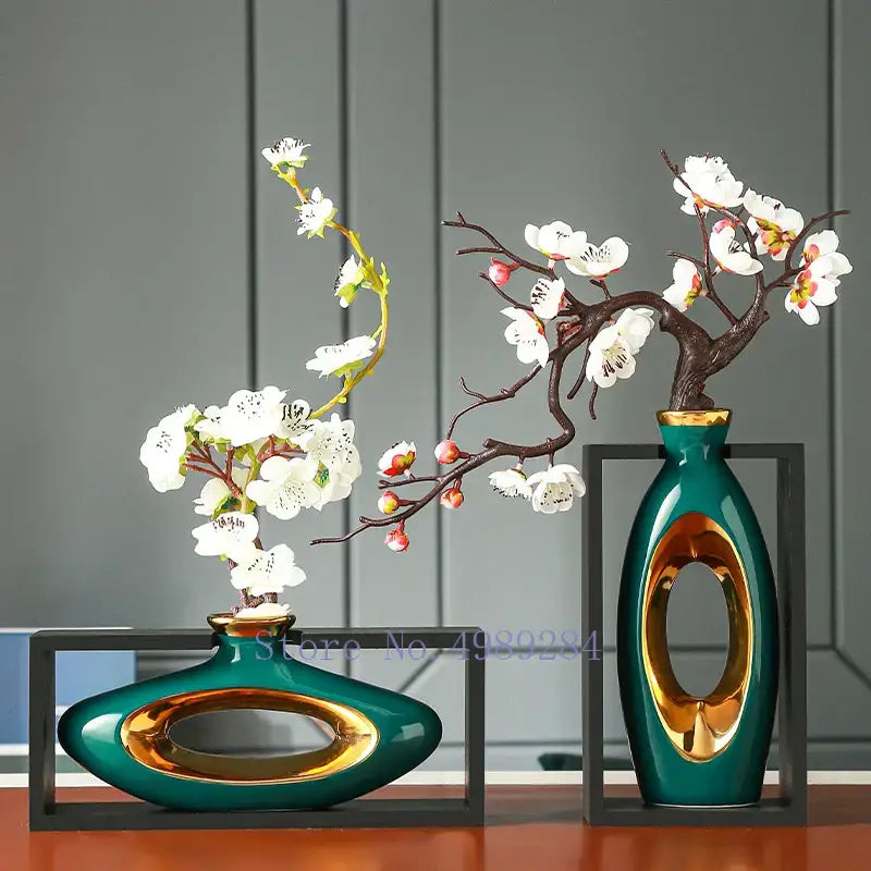 Two teal ceramic vases with gold oval cutouts holding white blossoms in decorbites chinese style ceramic wooden frame