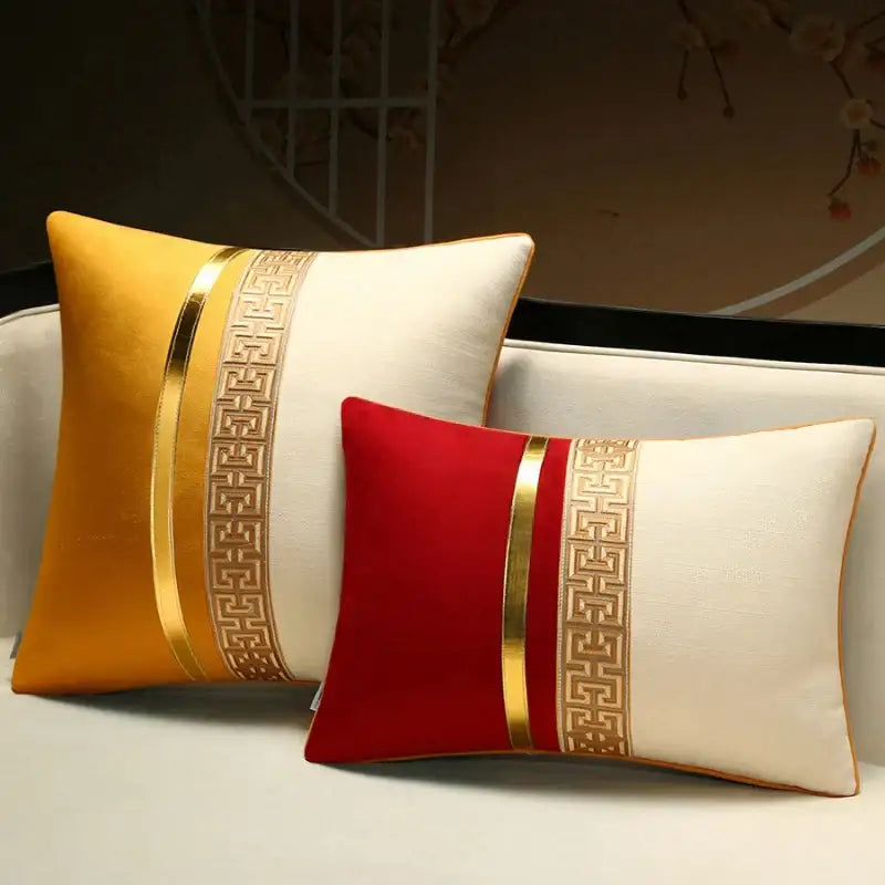 Two rectangular decorbites™ decorative pillow covers in golden yellow and red with cream panels and gold geometric borders