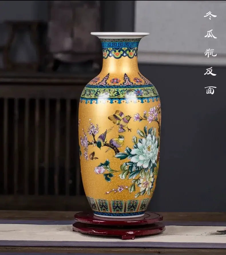 Golden porcelain enamel colored vase with intricate floral and bird motifs on red wooden stand by decorbites