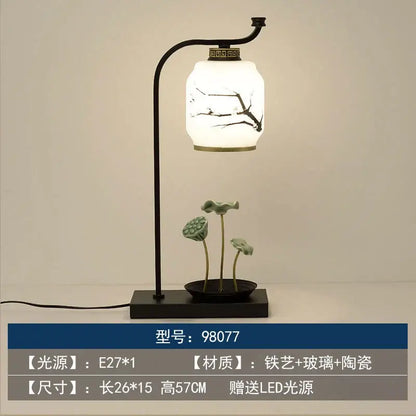 A sleek black iron decorbites chinoiserie table floor lamp with white glass shade and ceramic base featuring green lotus pods