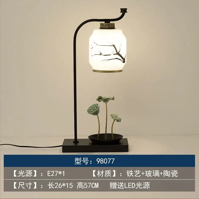 A sleek black iron decorbites chinoiserie table floor lamp with white glass shade and ceramic base featuring green lotus pods