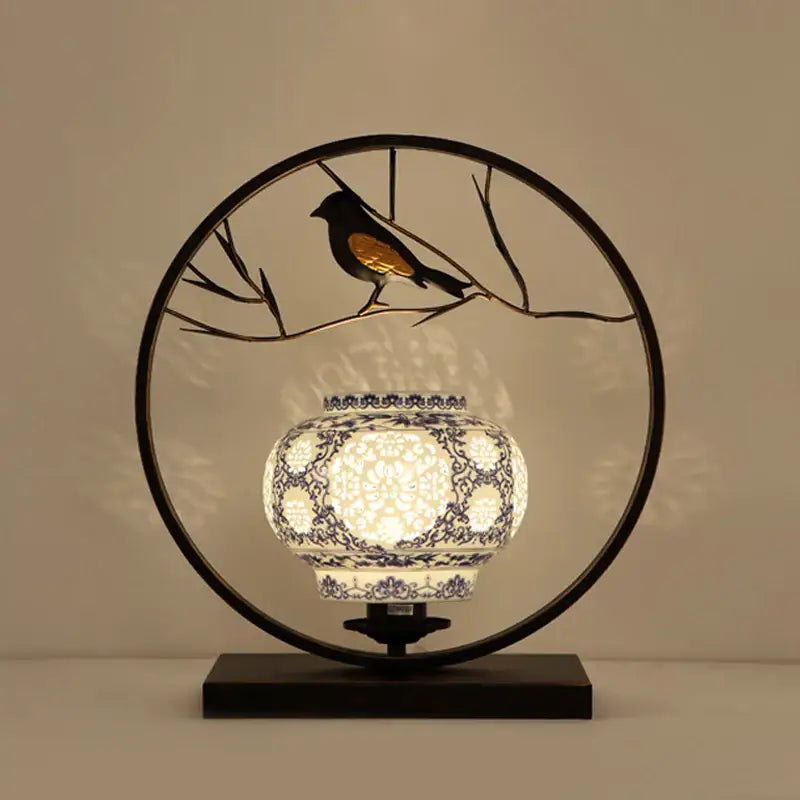 A glowing white ceramic DecorBites chinoiserie table floor lamp with blue floral patterns and black metal hoop frame