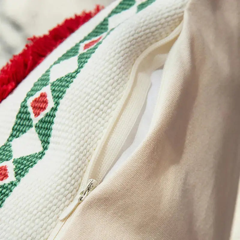 White cushion cover with green and red geometric embroidery, textured knit fabric, and handmade tassels for decorbites christmas decoration