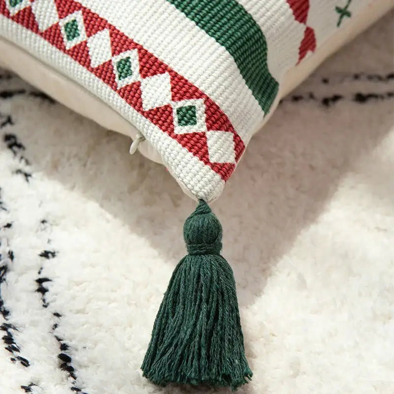 A cozy white cushion cover with red and green geometric embroidery and dark green tassel for DecorBites Christmas decoration
