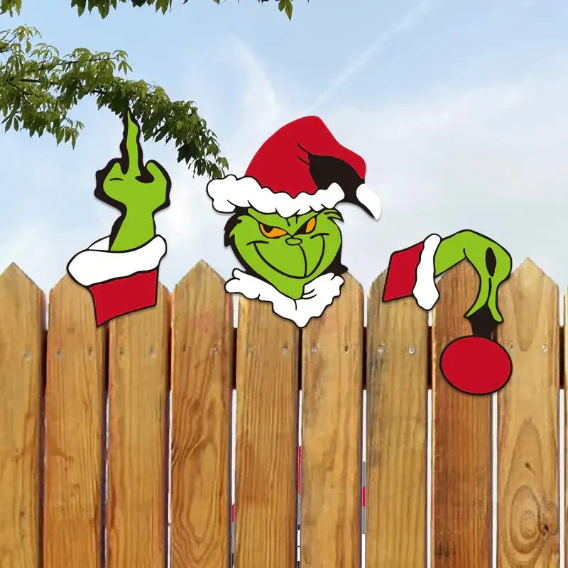Green grinch face with red santa hat peeking over wooden fence in decorbites christmas door frame set for festive decor