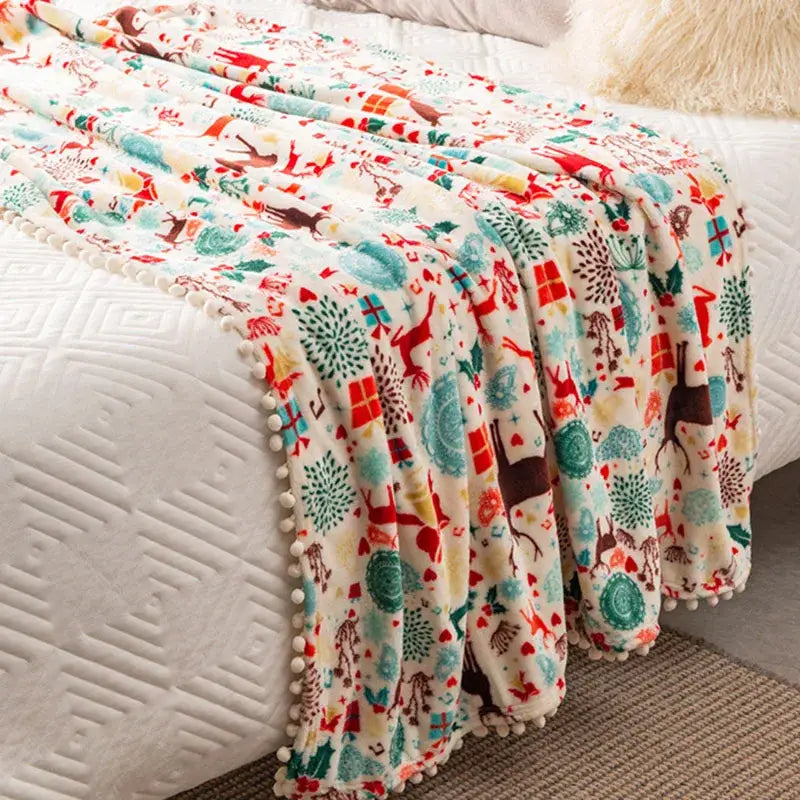 A cozy cream-colored decorbites christmas flannel blanket with festive motifs and plush pom-pom trim for winter use