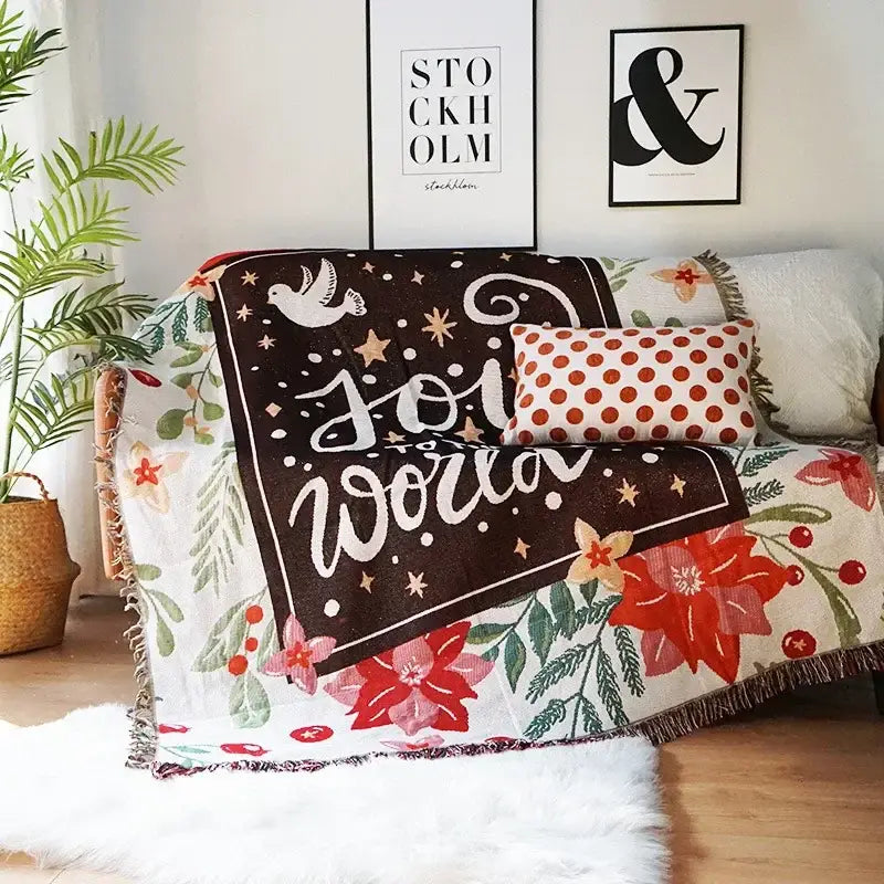 A decorbites christmas holiday sofa blanket with dark brown center text and star motifs bordered by red poinsettias and green foliage