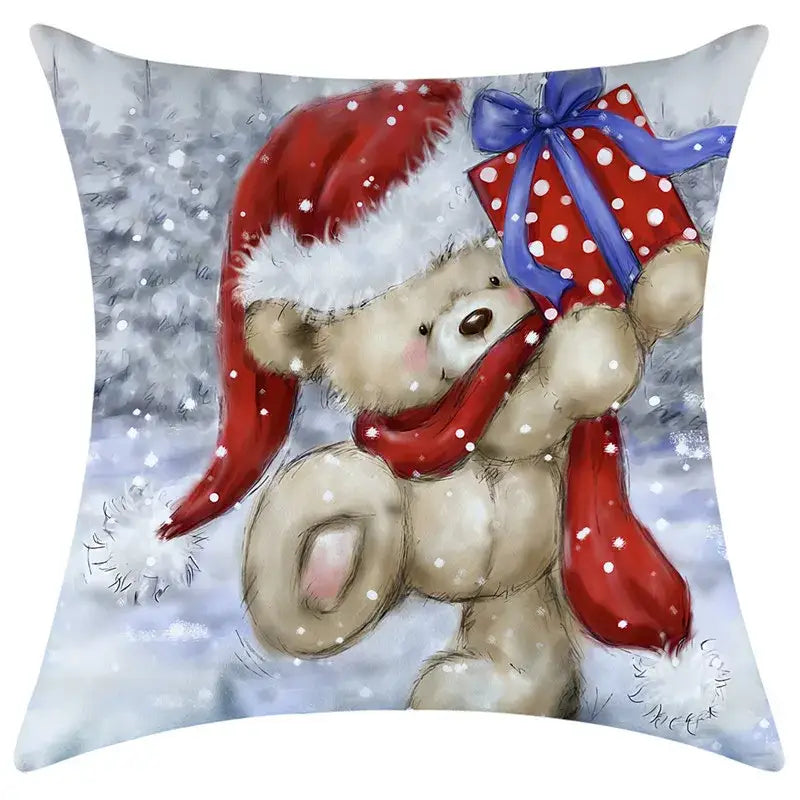 A cozy beige teddy bear wearing a red santa hat and scarf holding a gift on a decorbites christmas pillowcase