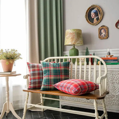 Three decorbites christmas plaid cushion covers in red green and blue tones on a wooden bench with white legs