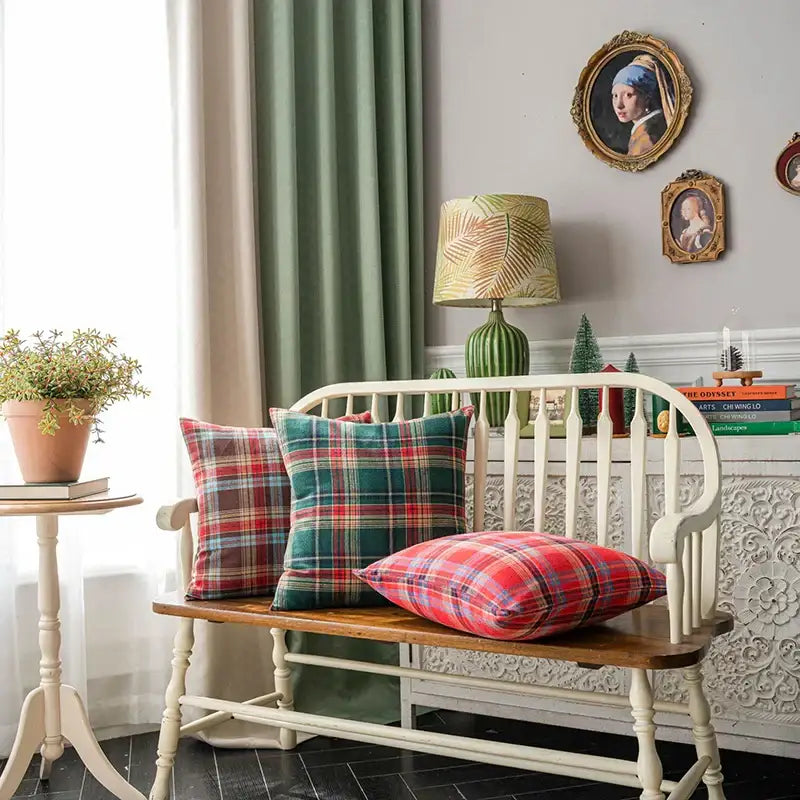 Three decorbites christmas plaid cushion covers in red green and blue tones on a wooden bench with white legs