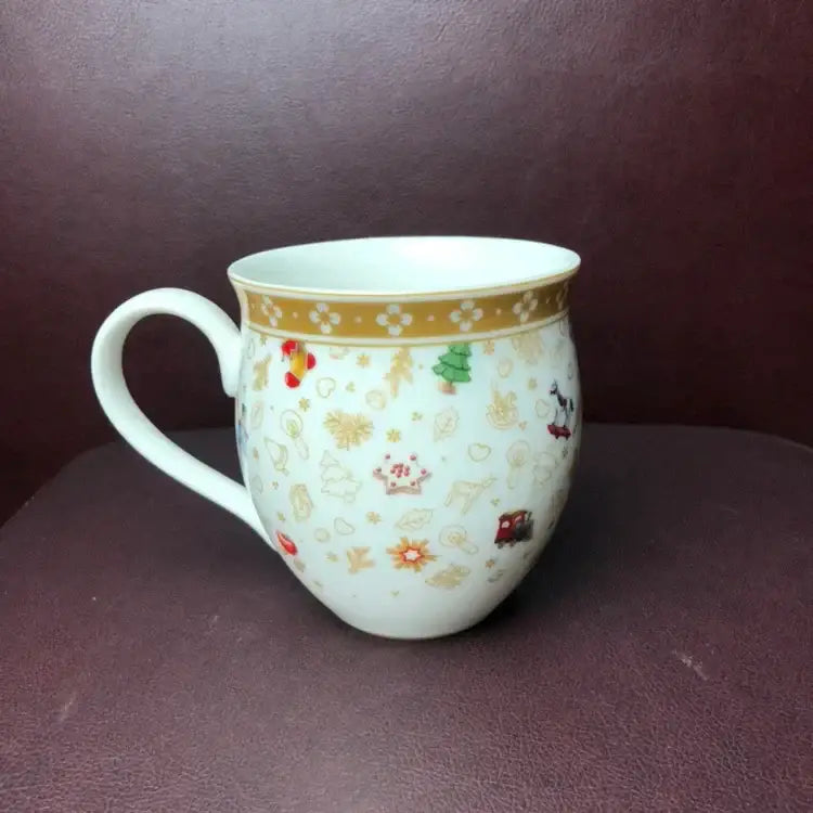 A white ceramic mug with festive gold red and green illustrations from the decorbites christmas porcelain tableware set