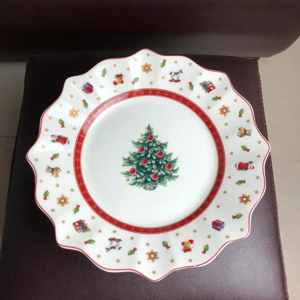White ceramic plate with scalloped edge featuring decorated christmas tree and festive illustrations in decorbites christmas porcelain tableware set