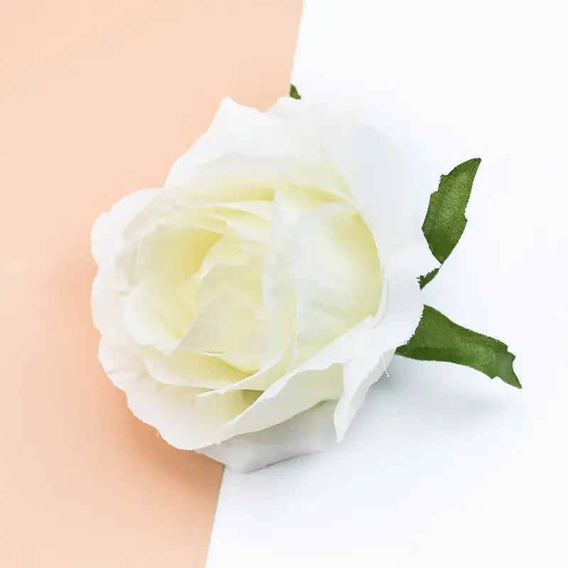 A delicate white artificial rose with soft layered petals and green fabric leaves in a decorbites christmas rose arch wall wreath
