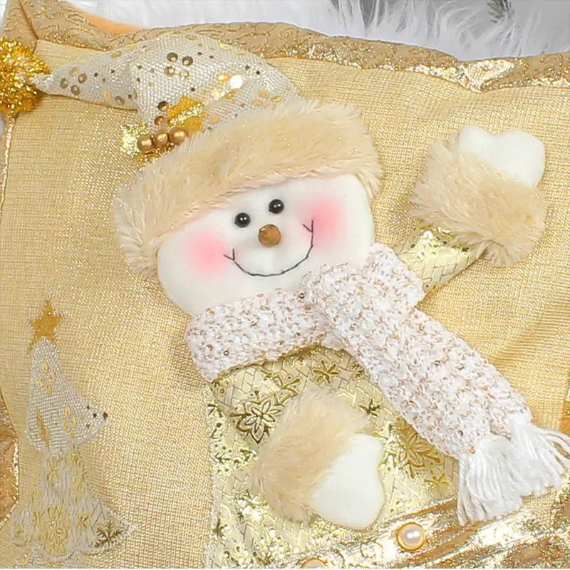 A plush snowman ornament with a beige hat and white scarf on a decorbites santa claus gold embroidered pillowcase