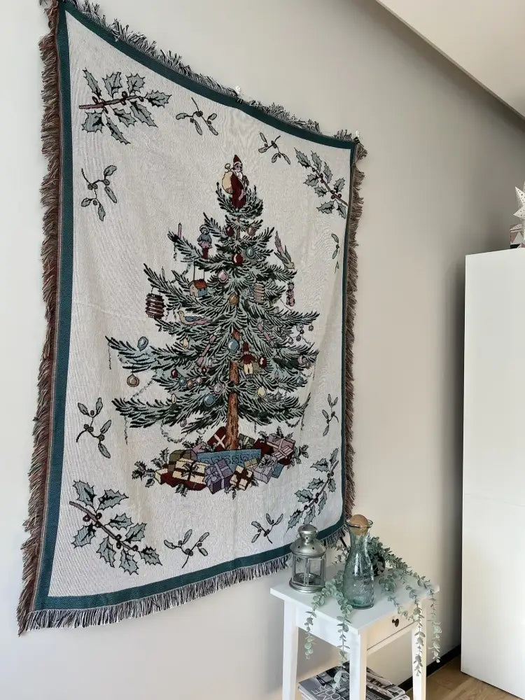 Cream-colored decorbites christmas throw blanket with woven christmas tree design framed by dark green borders and fringes