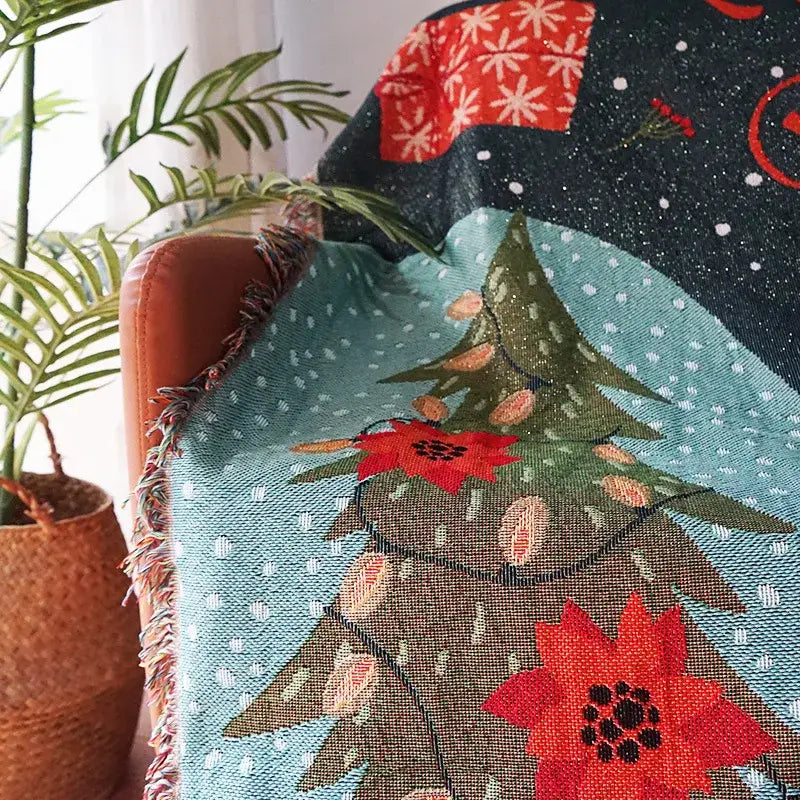 A cozy teal decorbites christmas tree knitted throw blanket with red poinsettias snowflakes and fringed edges