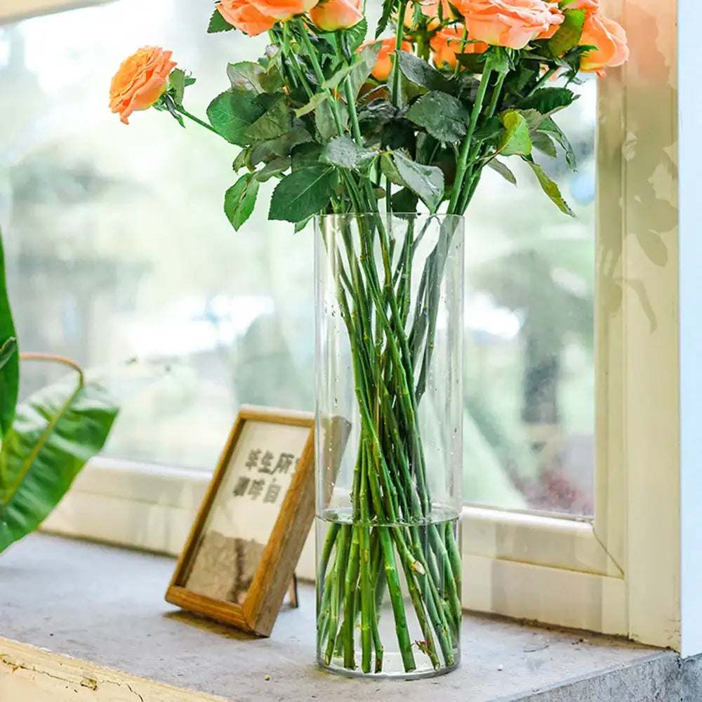 DecorBites™ clear acrylic hurricane flower vase large size holding vibrant orange roses with green stems and leaves