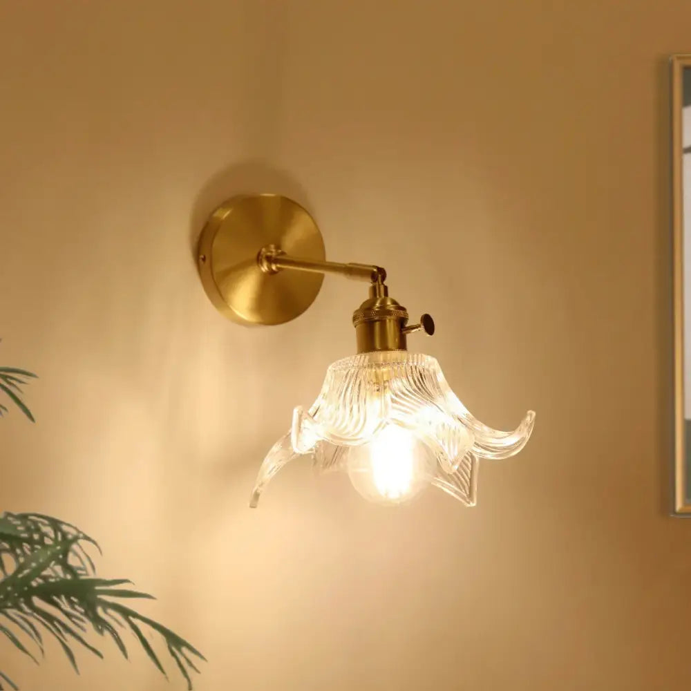 A brass wall lamp with a decorbites clear flower glass petal-shaped shade and a pull chain for bedroom use