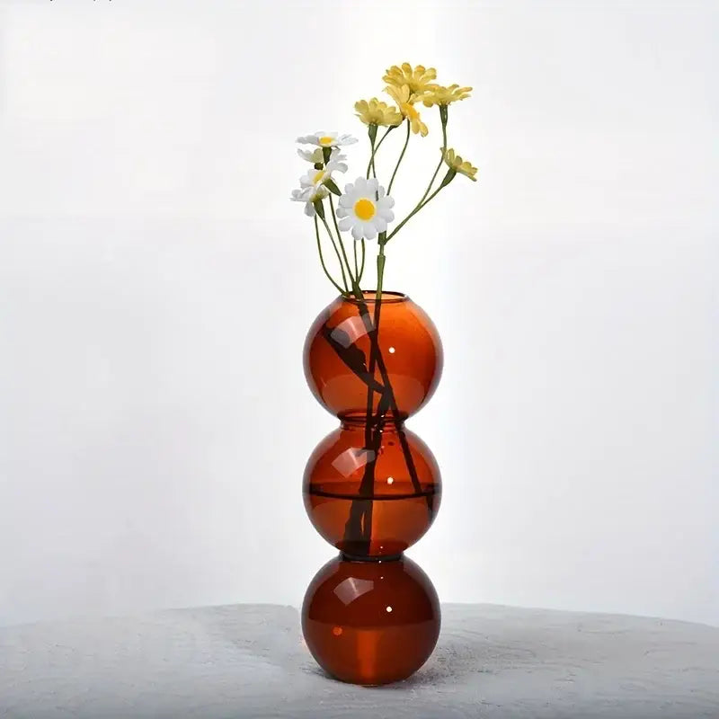 Decorbites clear glass bubble vase in translucent amber with three stacked spheres holding white and yellow daisies for home decor