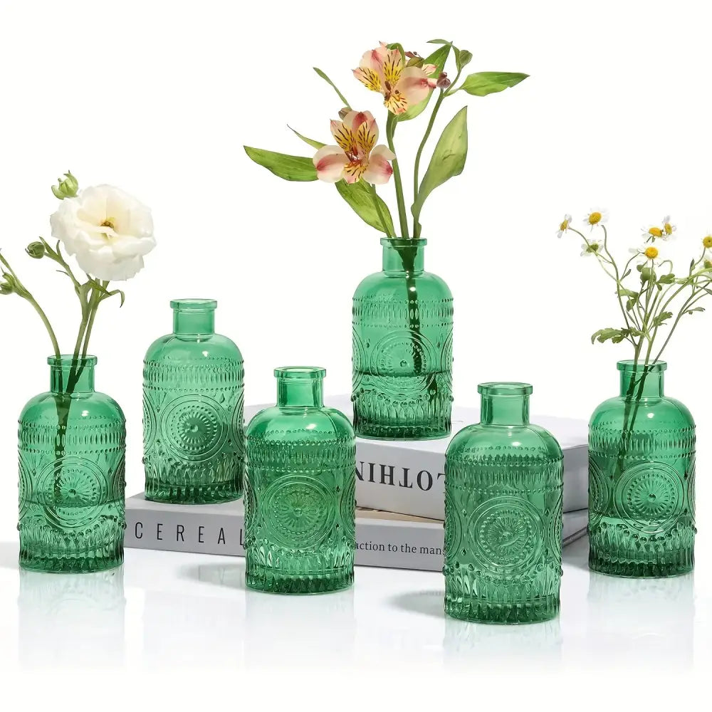 Set of five emerald green clear glass bud vases with embossed patterns and ribbed necks holding delicate flowers
