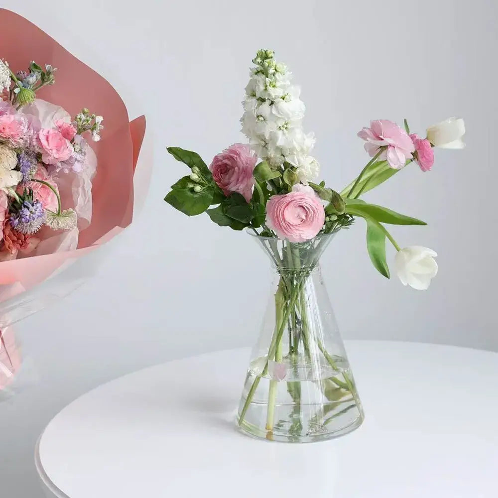 Clear nordic plastic vase with flared rim holding pink ranunculus and tulips for hydroponic flowers display