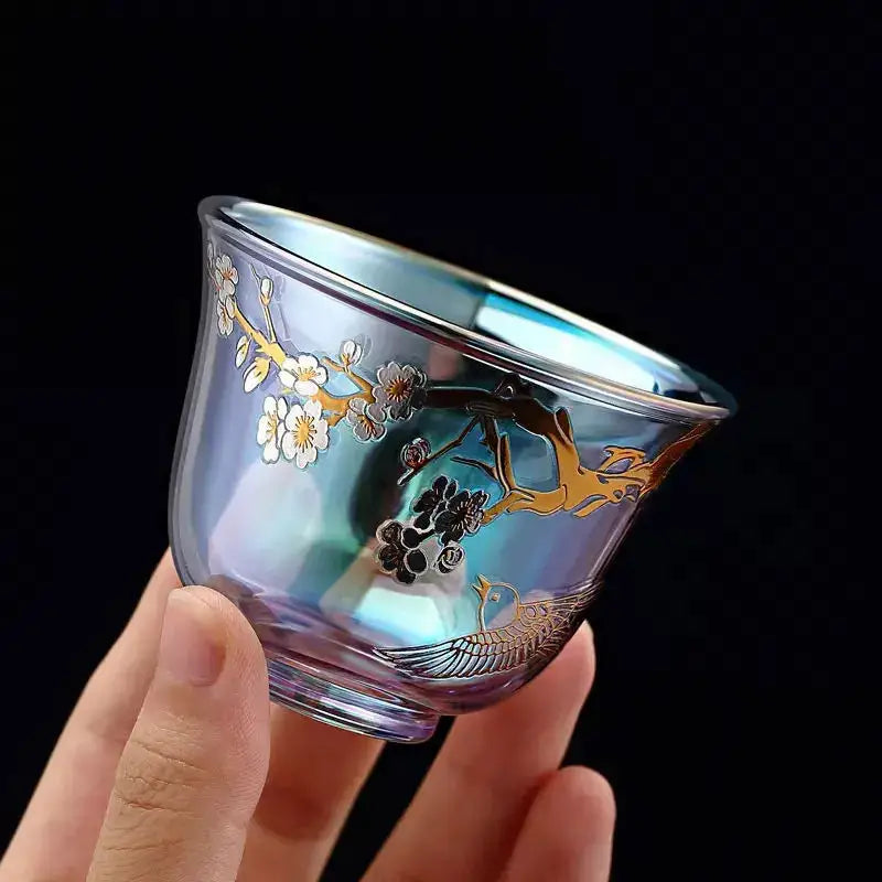 A translucent iridescent glass teacup with colorful enamel floral and bird design held in hand by decorbites colorful enamel