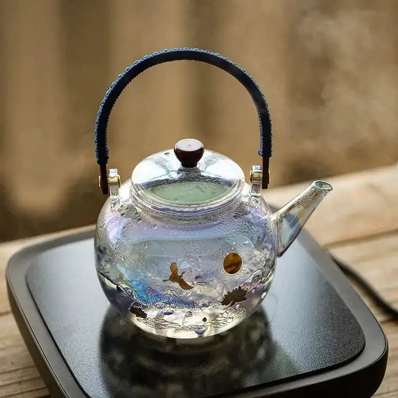 A colorful enamel glass teapot by Decorbites with blue braided handle gold accents and painted crane and lotus decor