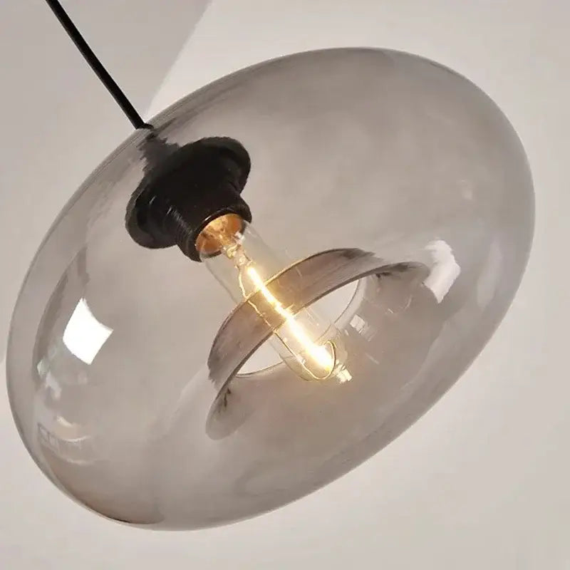A sleek smoked glass colorful led pendant light with black cord and exposed filament bulb for restaurant decor