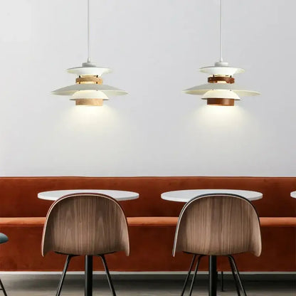Two white and wood-toned decorbites colorful umbrella led chandeliers with modern tiered design hang above tables