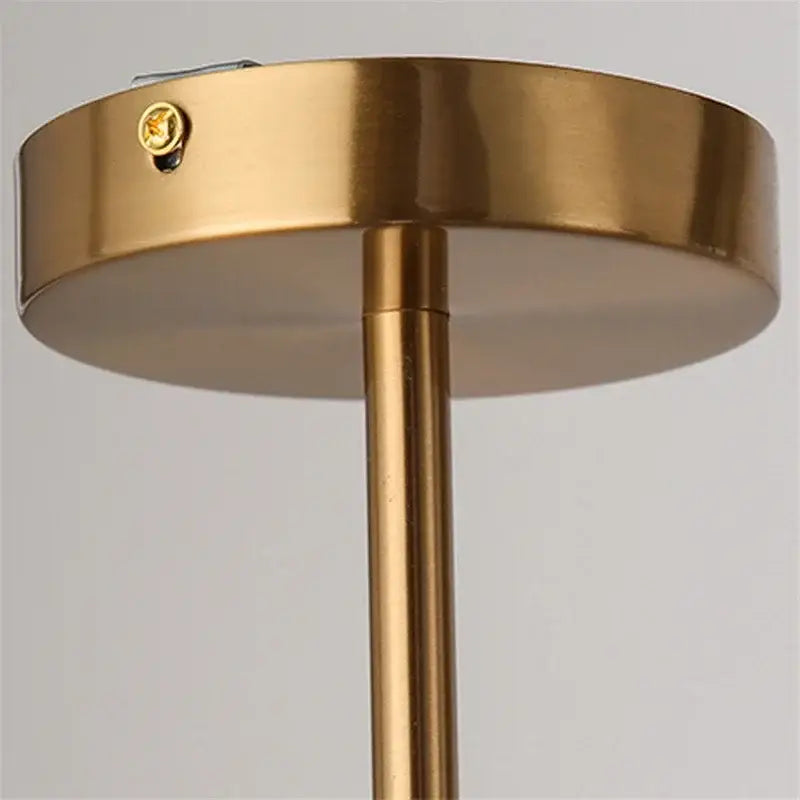 Gold-finished metal ceiling light fixture with circular base and slender stem featuring a white glass ball shade