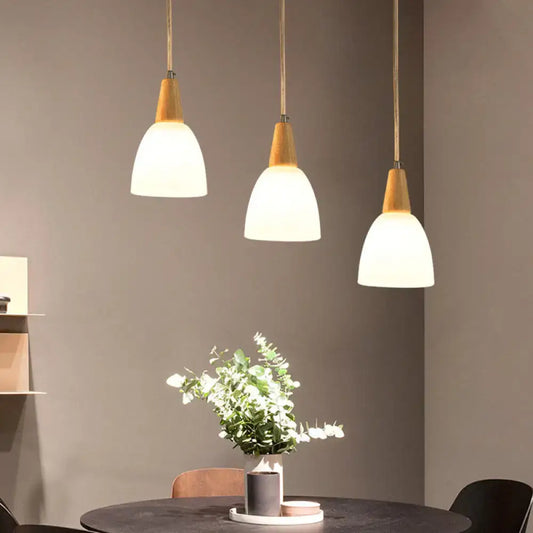 Three modern pendant lights with warm wooden tops and frosted glass dome shades in a minimalist dining space