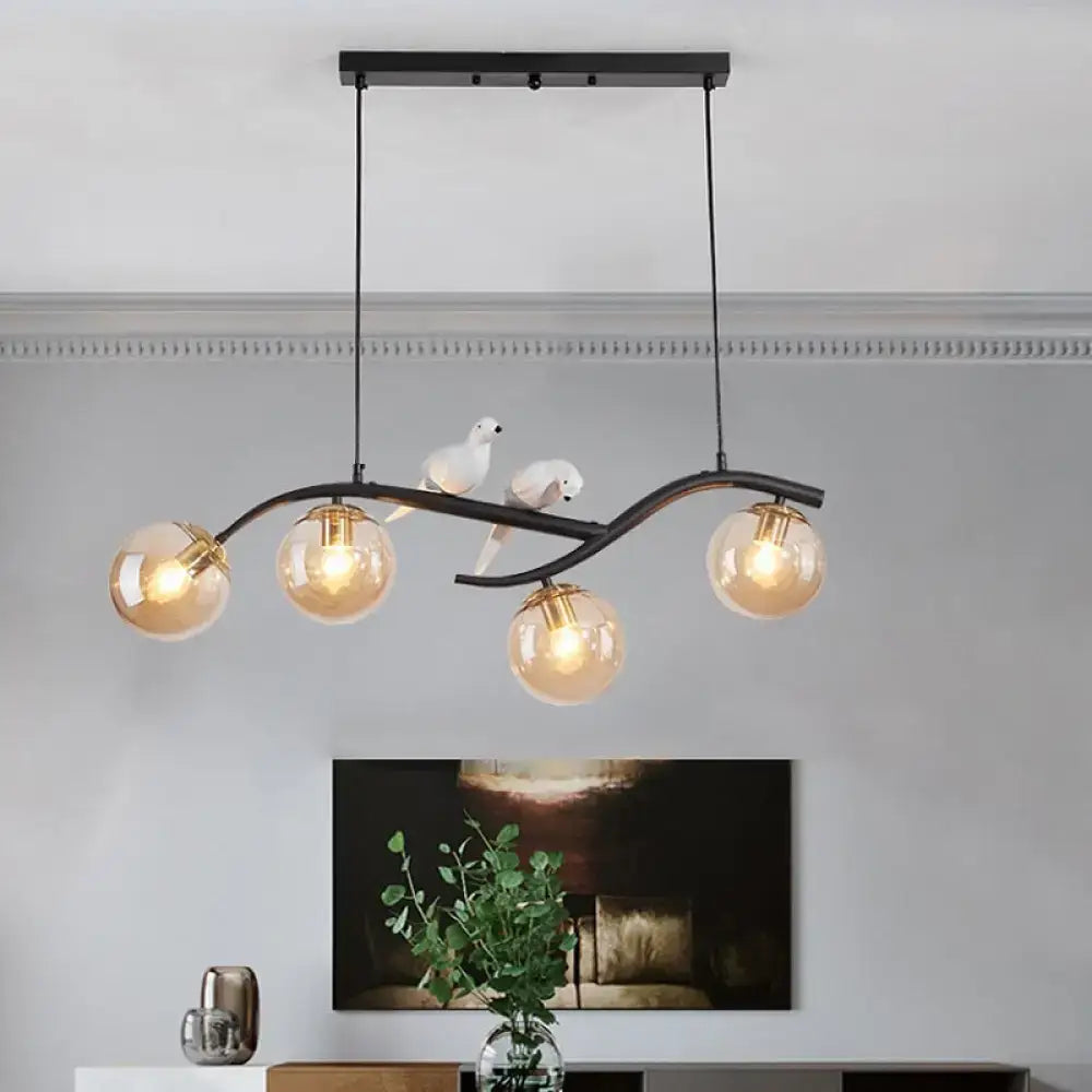 Black metal chandelier with curved branch design featuring four amber glass globes and bird decor in smoke grey cognac tones