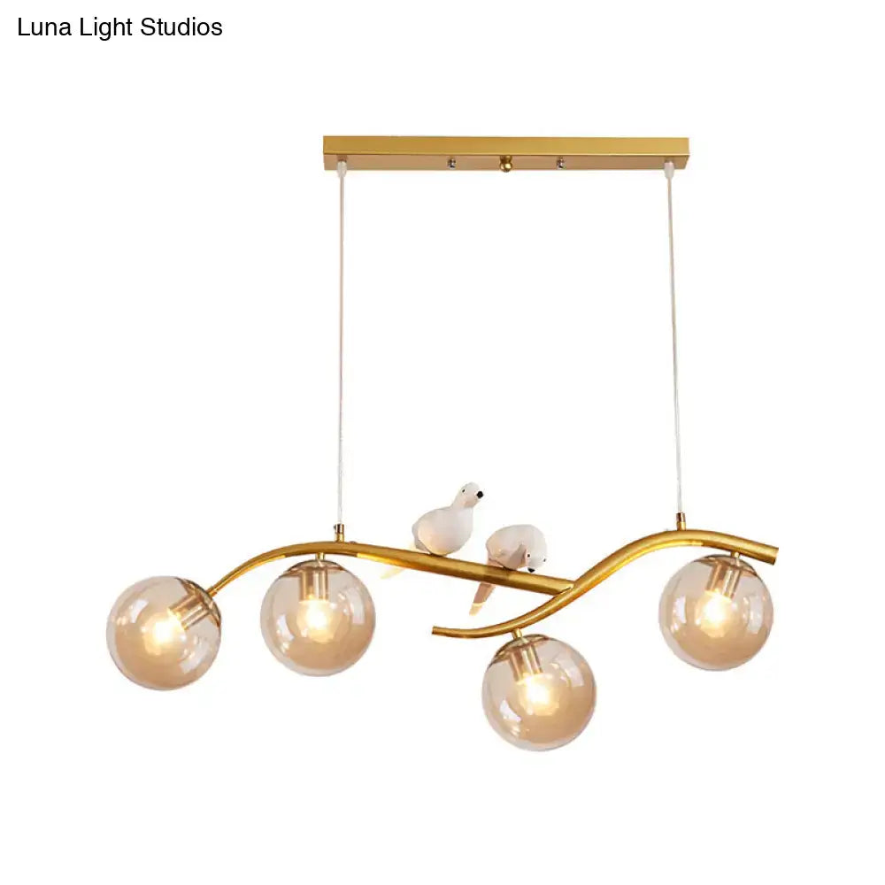 Gold-toned DecorBites™ pendant light with curved branch design, four amber glass globes, white birds, smoke grey cognac shades