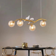 Gold-toned metal branch pendant light with four smoke grey cognac glass bulbs and white ceramic bird decor by DecorBites