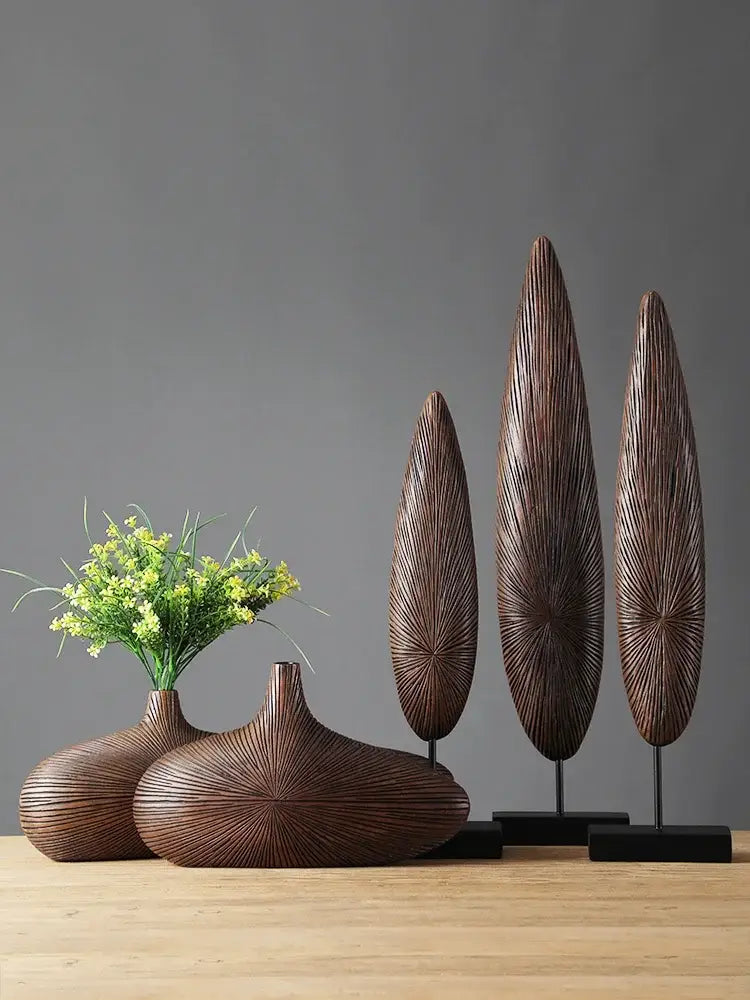 Dark brown intricately ribbed wooden sculptures paired with a contemporary resin vase for flower arrangements