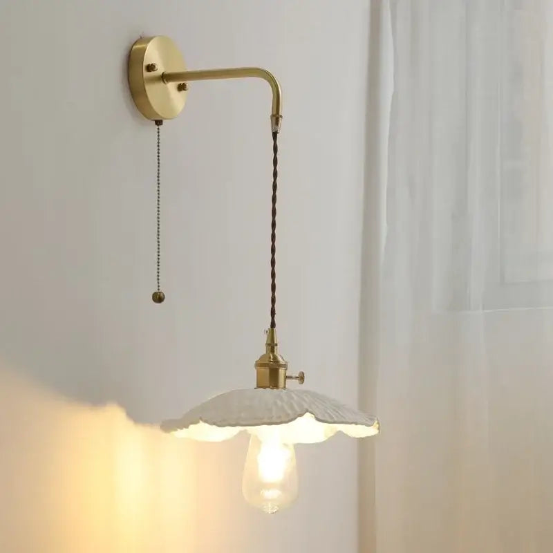 A vintage brass wall light with a curved arm, dark braided cord, and off-white ceramic led wall lampshade