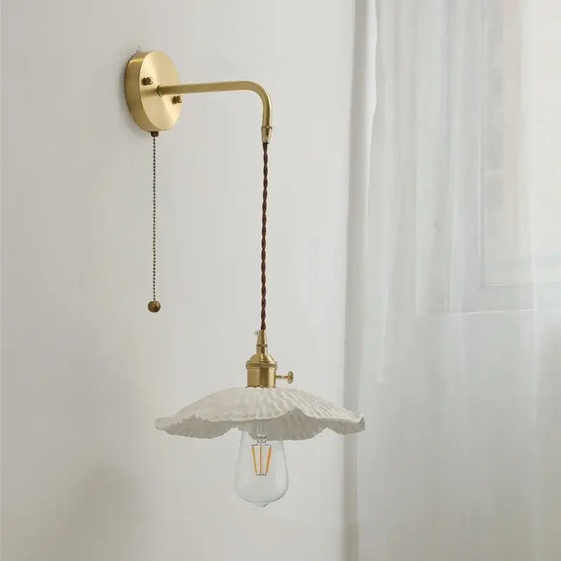 A vintage brass and white ceramic led wall light with a fluted petal design hanging from a chain fixture